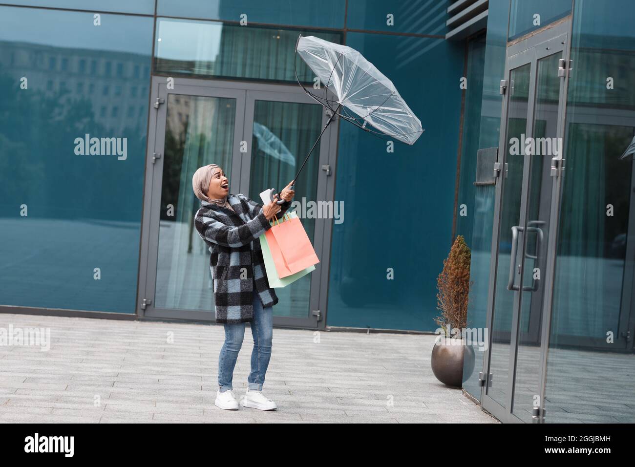 À pied du centre commercial et des magasins. Femme essayant de garder son parapluie sous le vent fort Banque D'Images