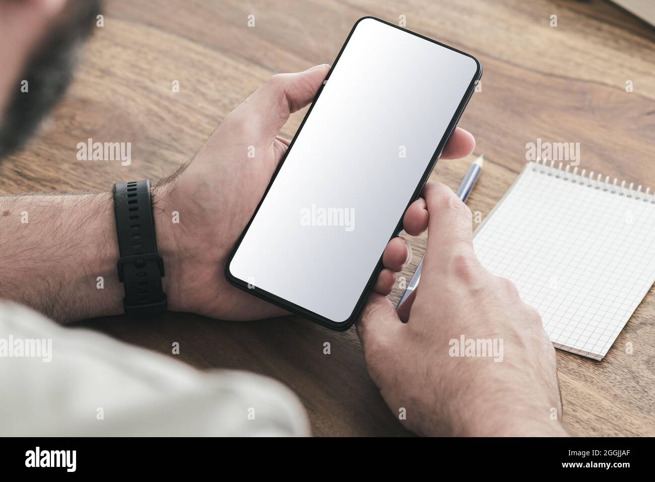 vue sur l'épaule d'un homme assis à une table en bois à l'aide d'un smartphone Banque D'Images