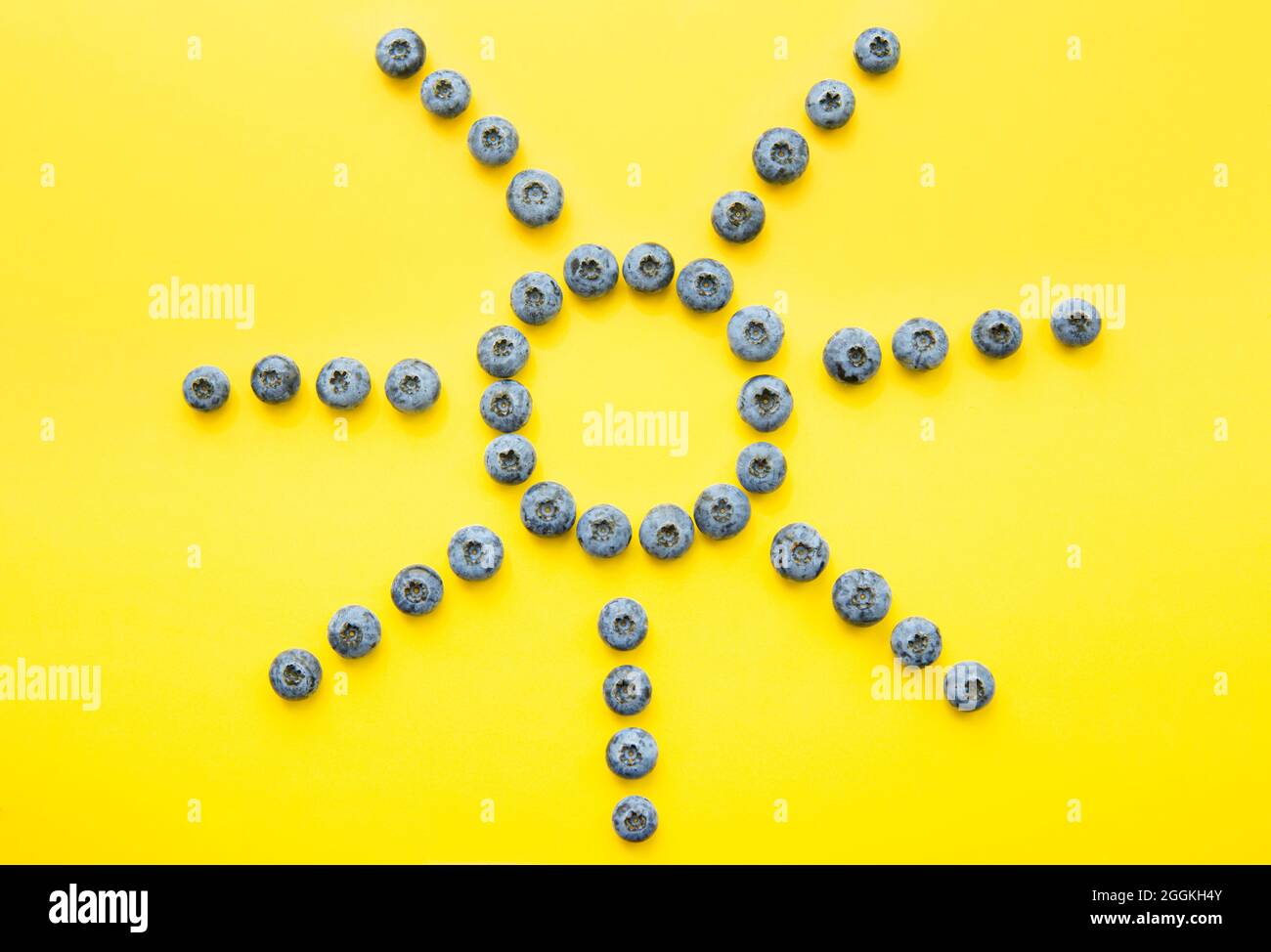 Bleuets disposés en forme de soleil sur fond jaune Banque D'Images