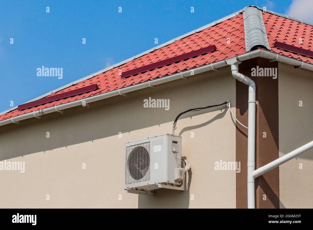 Air conditionné suspendu à l'extérieur sur le mur d'un bâtiment ou d'une maison moderne à côté du toit contre un ciel bleu. Banque D'Images