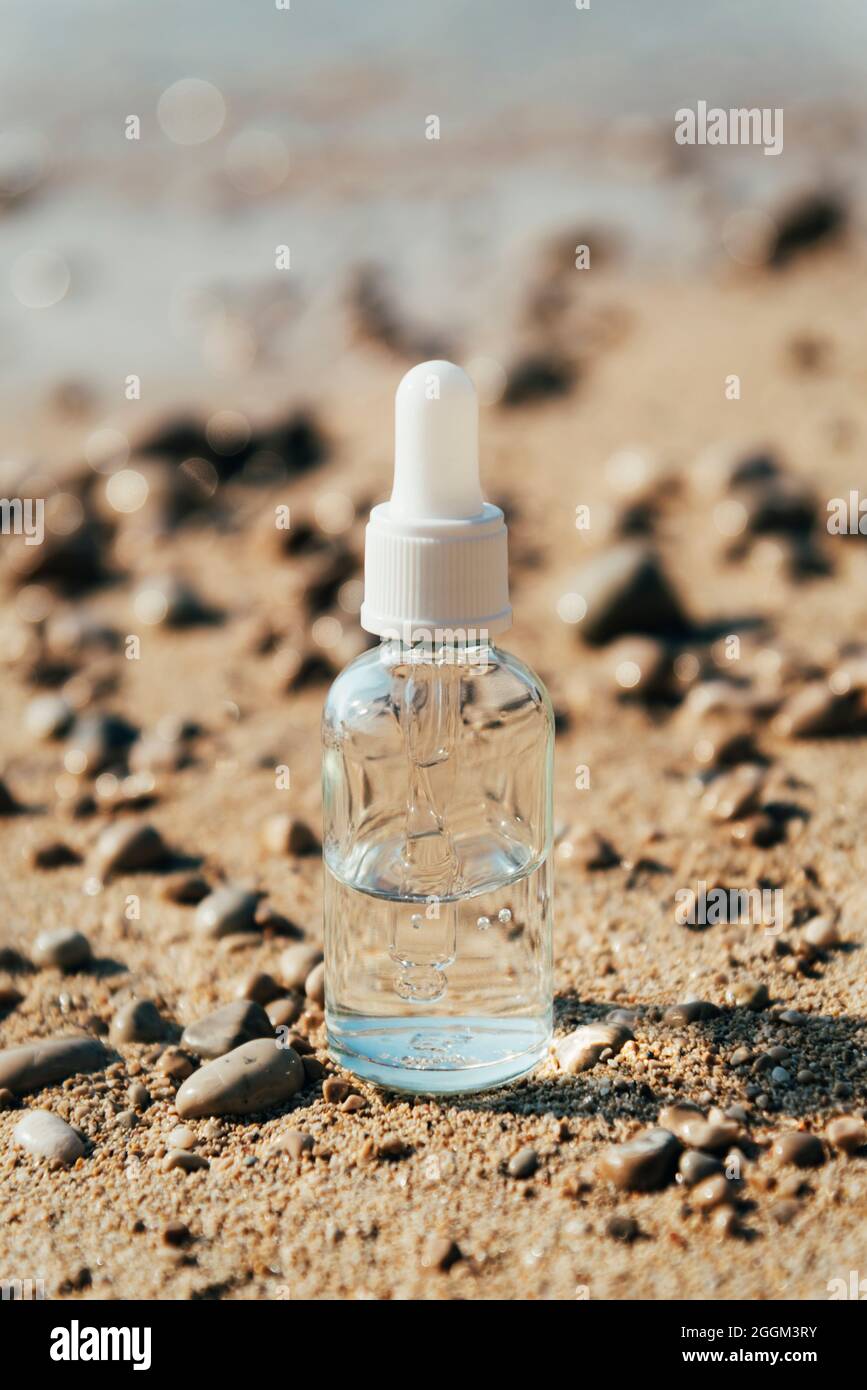 Hydratant cosmétique, bouteille d'huile ou de sérum dans le sable de plage. Cosmétiques naturels, concept de vacances d'été. Gros plan. Banque D'Images