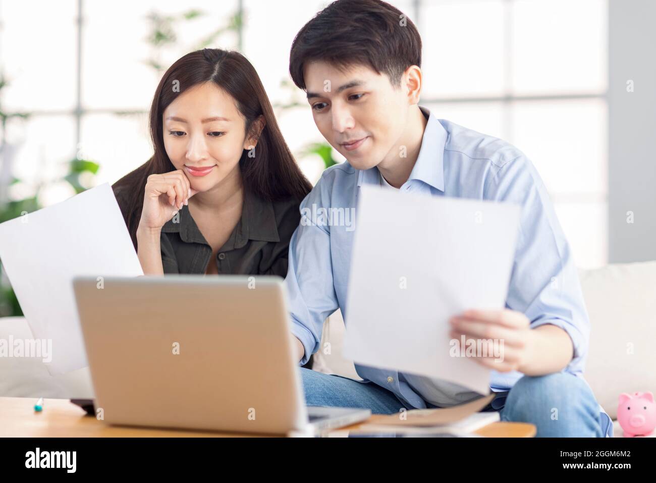 Un jeune mari et une jeune femme qui tient des documents administratifs et qui utilisent un ordinateur portable à la maison. Banque D'Images