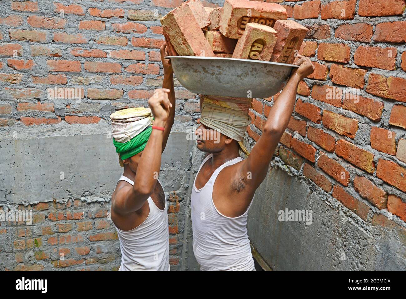 Main-d'œuvre transportant de la brique sur la tête du chantier Banque D'Images