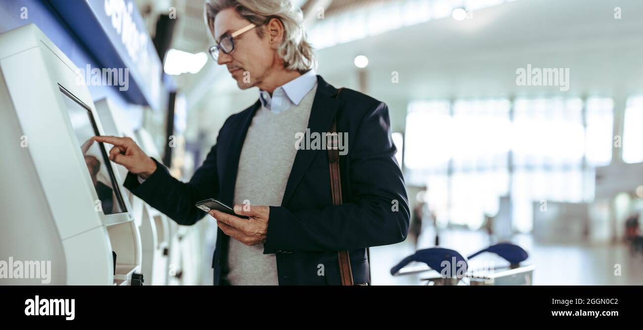 Un cadre d'affaires mature utilisant un enregistrement pratique en libre-service à l'aéroport. Le voyageur d'affaires utilise l'enregistrement en libre-service à l'aéroport. Banque D'Images