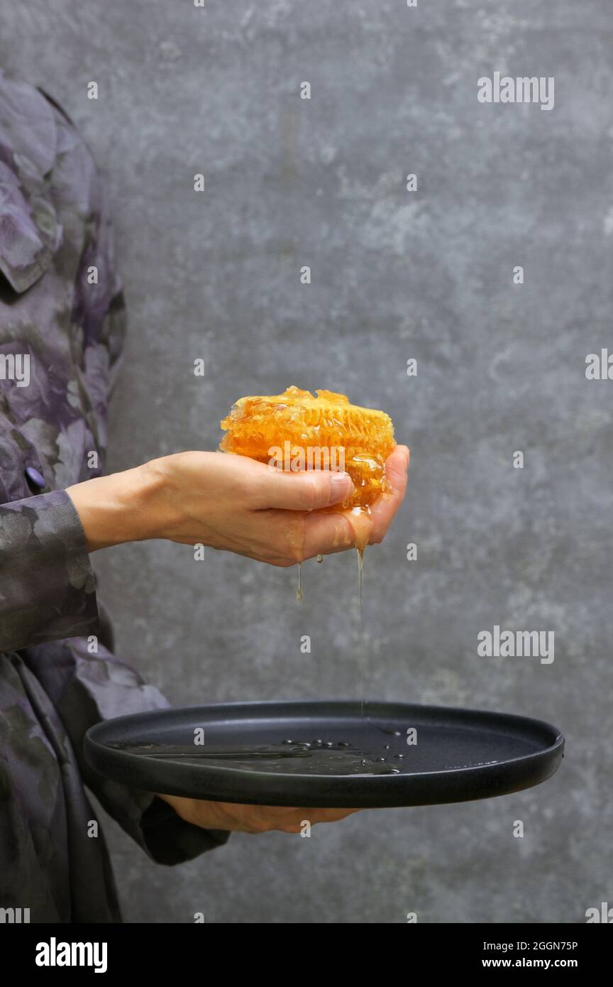 Main féminine Holdong miel frais en nid d'abeille sur plaque Banque D'Images
