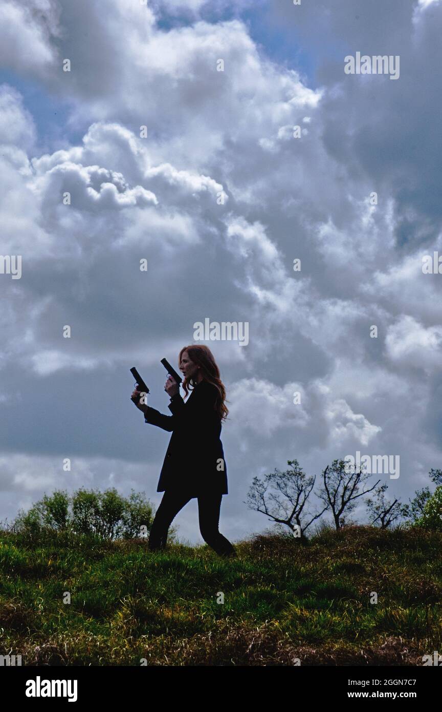 livre style de couverture femme seule silhouette de femme avec des armes à feu à l'horizon avec de grands nuages derrière elle. Banque D'Images