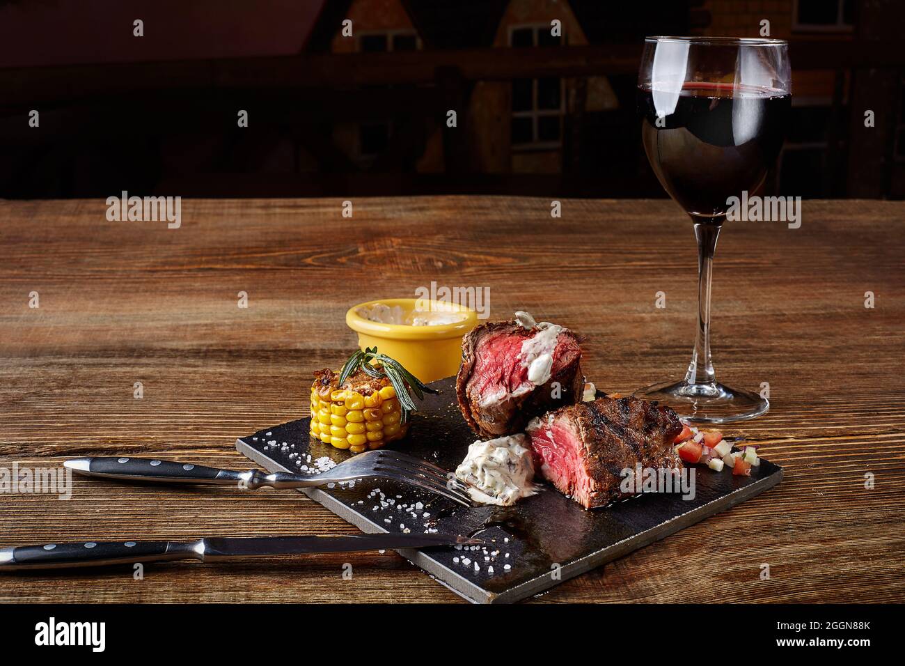 Steak barbecue avec un verre de vin rouge en gros plan sur tableau noir sur fond de bois Banque D'Images