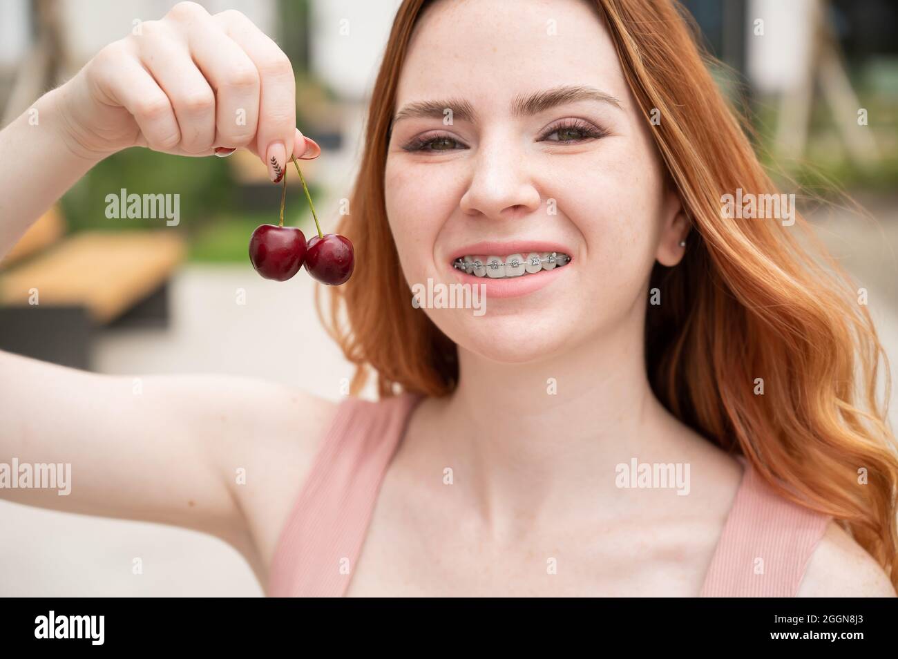Belle jeune femme aux cheveux rouges avec des bretelles sur ses dents mange  des cerises douces en plein air en été Photo Stock - Alamy