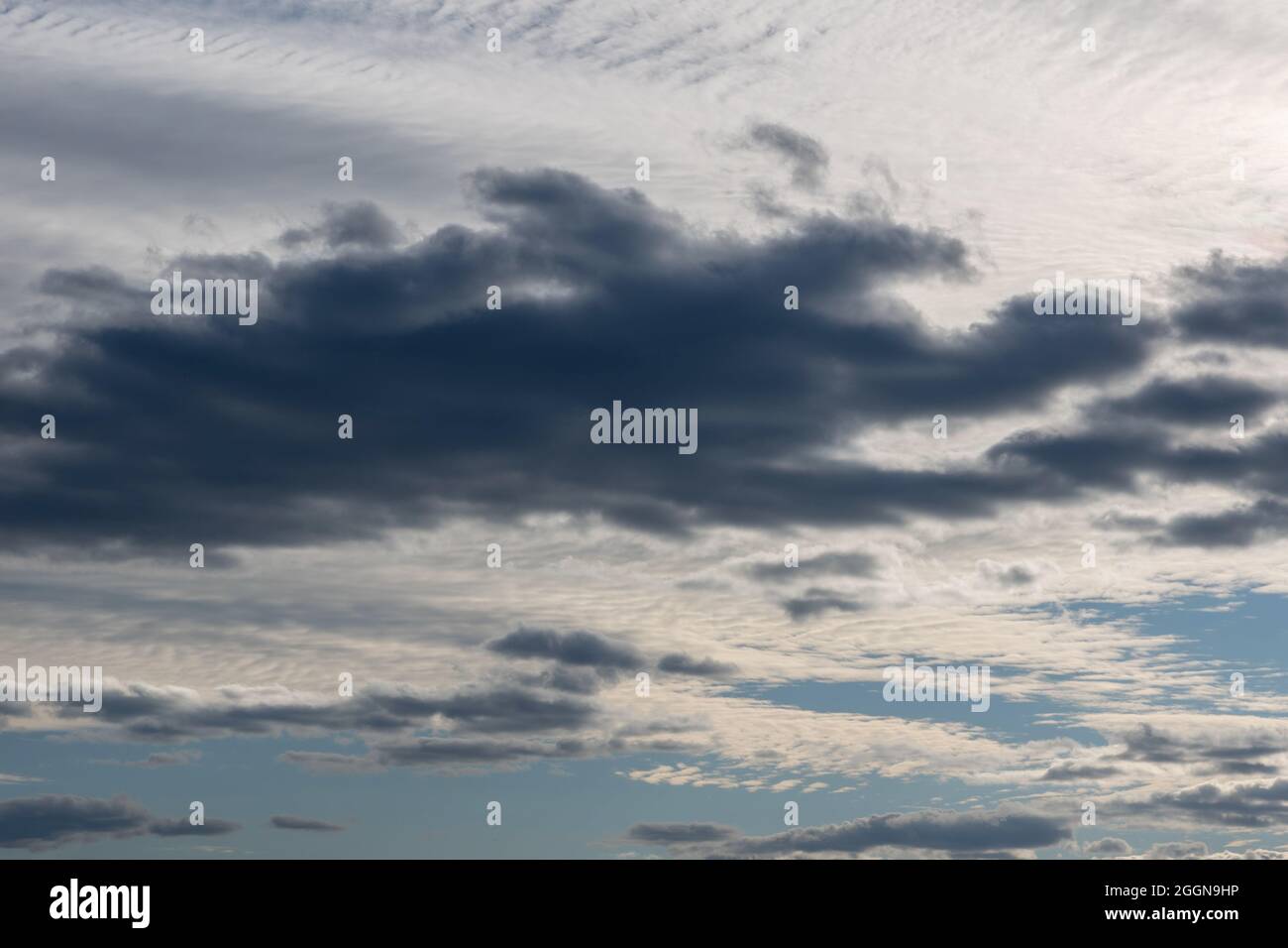 Nuages gris-blanc dans le ciel illuminés par le soleil couchant. Ciel bleu clair derrière des nuages de tempête sombres et spectaculaires. Fond de ciel naturel parfait, moc Banque D'Images