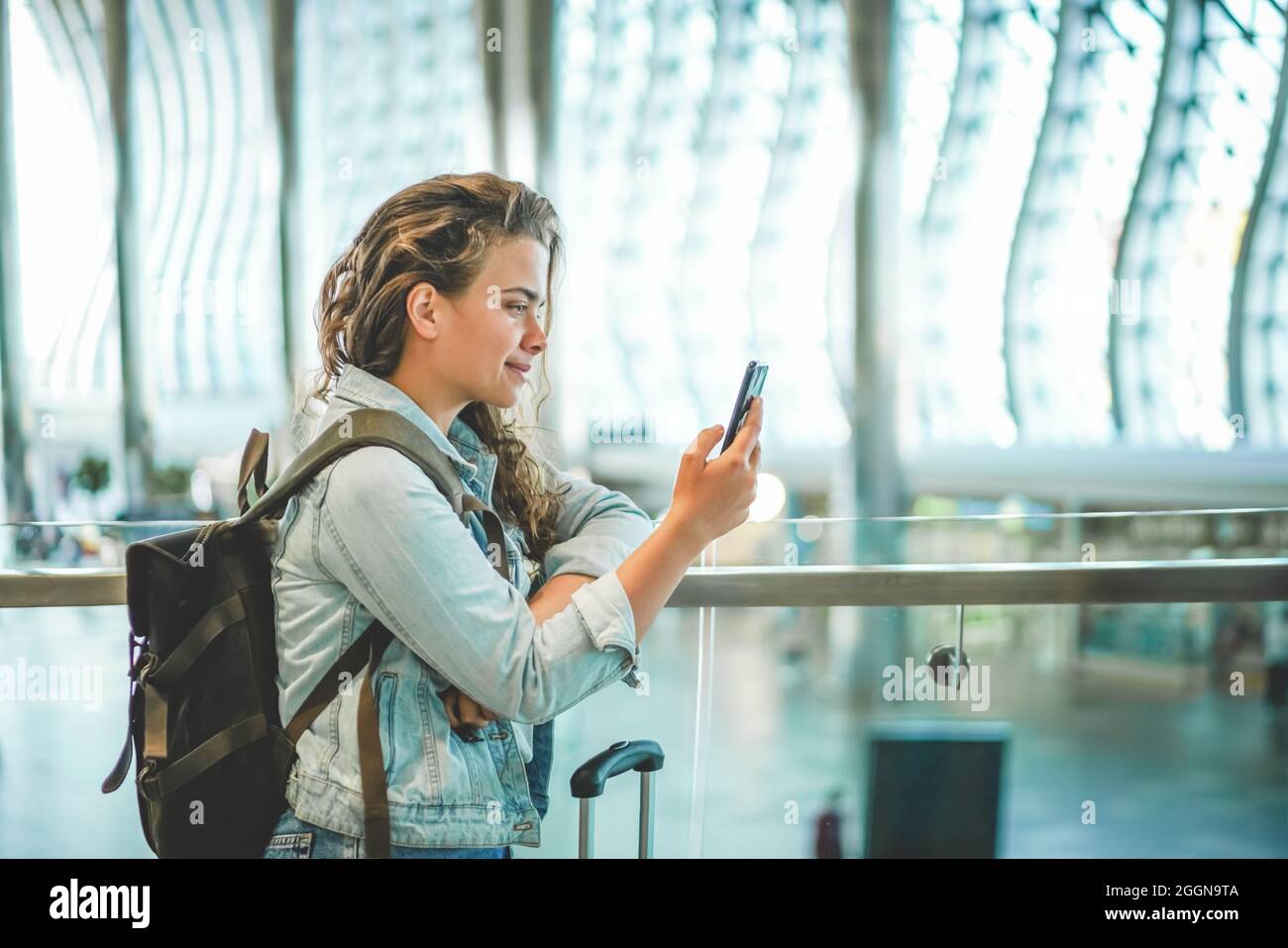 Une belle jeune femme caucasienne utilisant un téléphone portable à l'aéroport pour acheter des billets en ligne, réserver un hôtel, ou louer une voiture. Le temps de Covid voyage, l'espace pour le texte Banque D'Images