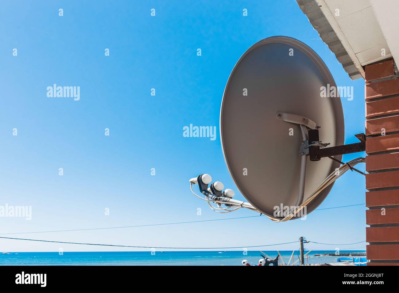 Antenne TV satellite sur le balcon de la maison avec vue sur la mer contre le ciel bleu. Banque D'Images