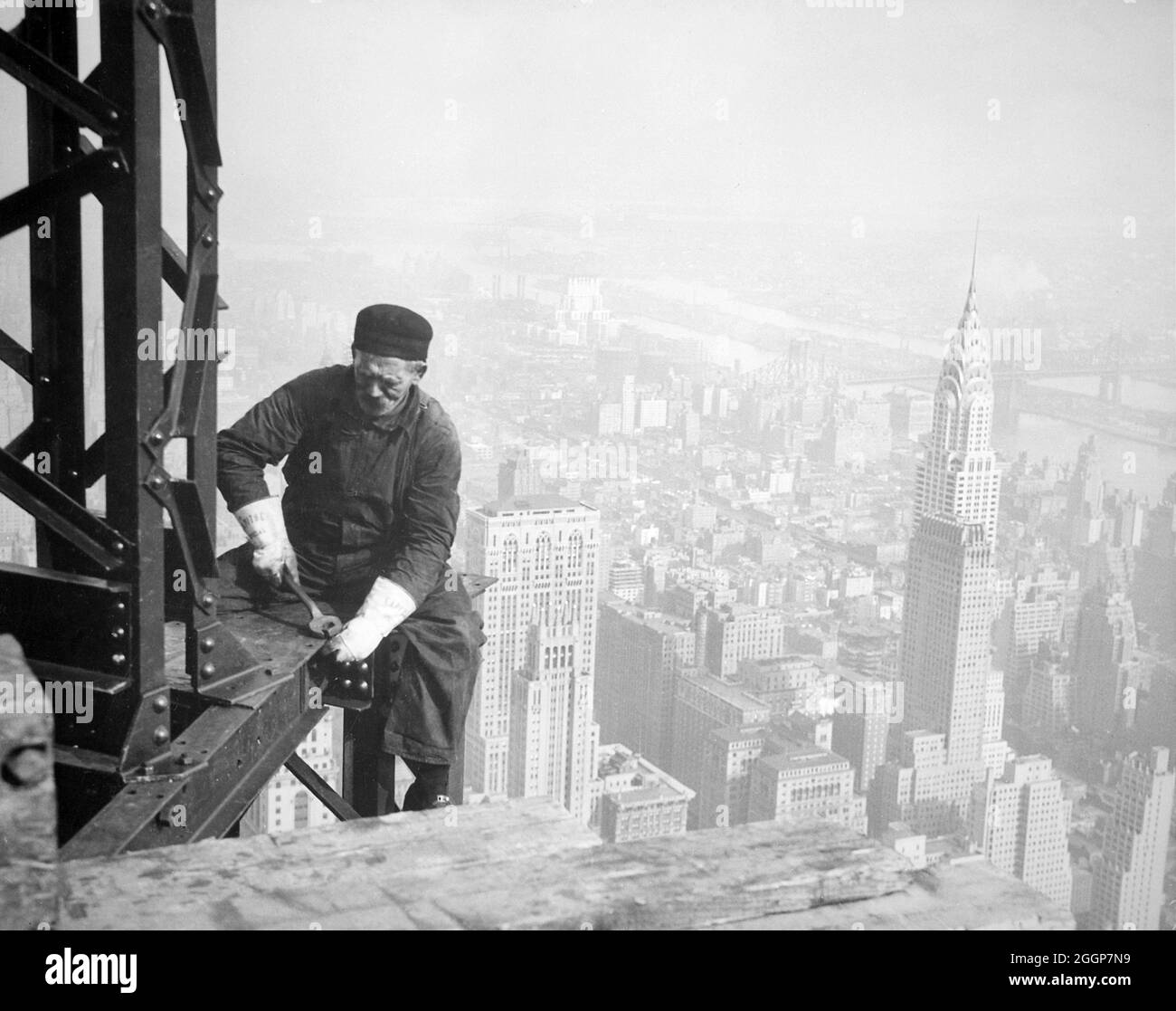 Un ouvrier sur le cadre de l'Empire State Building à New York, avec le Chrysler Building en arrière-plan, vers 1930. Banque D'Images