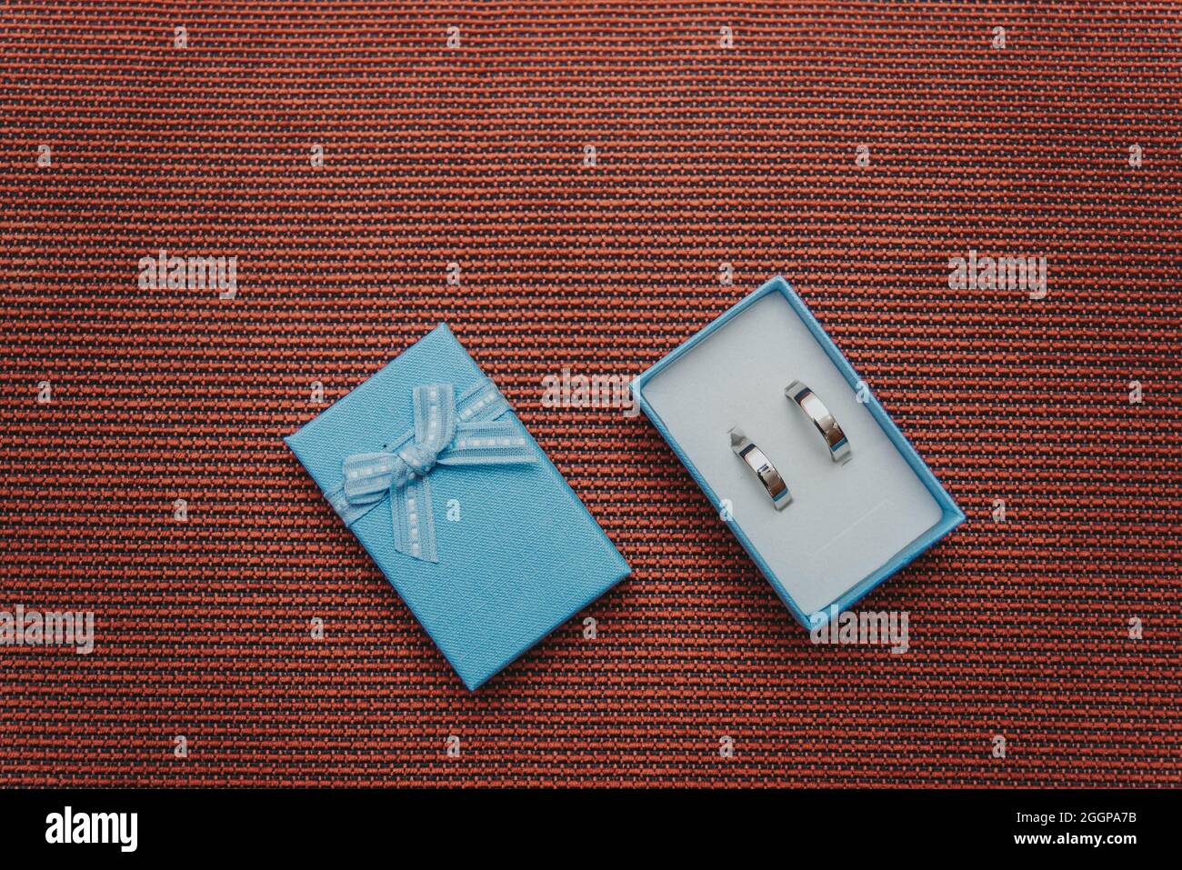 anneaux de mariage dans une boîte bleue sur fond rouge texturé vue du dessus Banque D'Images