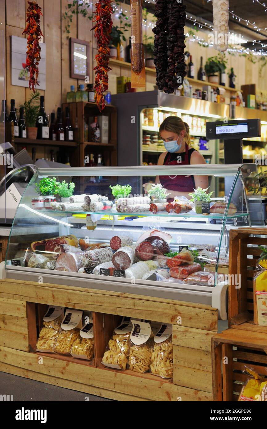 Jeune femme servant au comptoir local de charcuterie vendant une variété de saucisses et de produits de viande avec des piments séchés et de l'ail accrochés par le dessus Banque D'Images