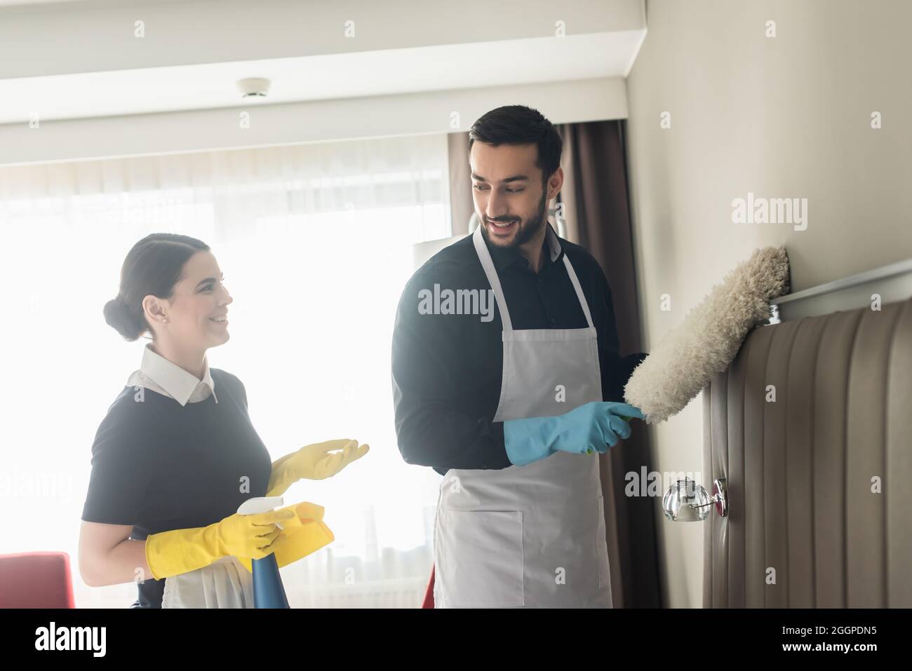 les femmes de ménage se regardent les unes les autres tout en tenant les fournitures de nettoyage et le nettoyage de la chambre d'hôtel Banque D'Images