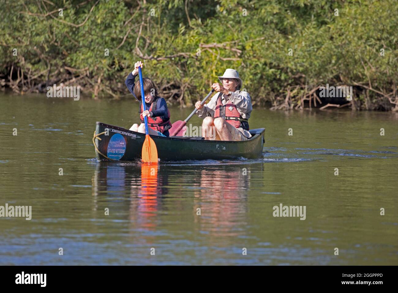 Homme âgé et jeune garçon pagayant le canoë canadien sur la rivière Wye Hoarwithy, Royaume-Uni Banque D'Images
