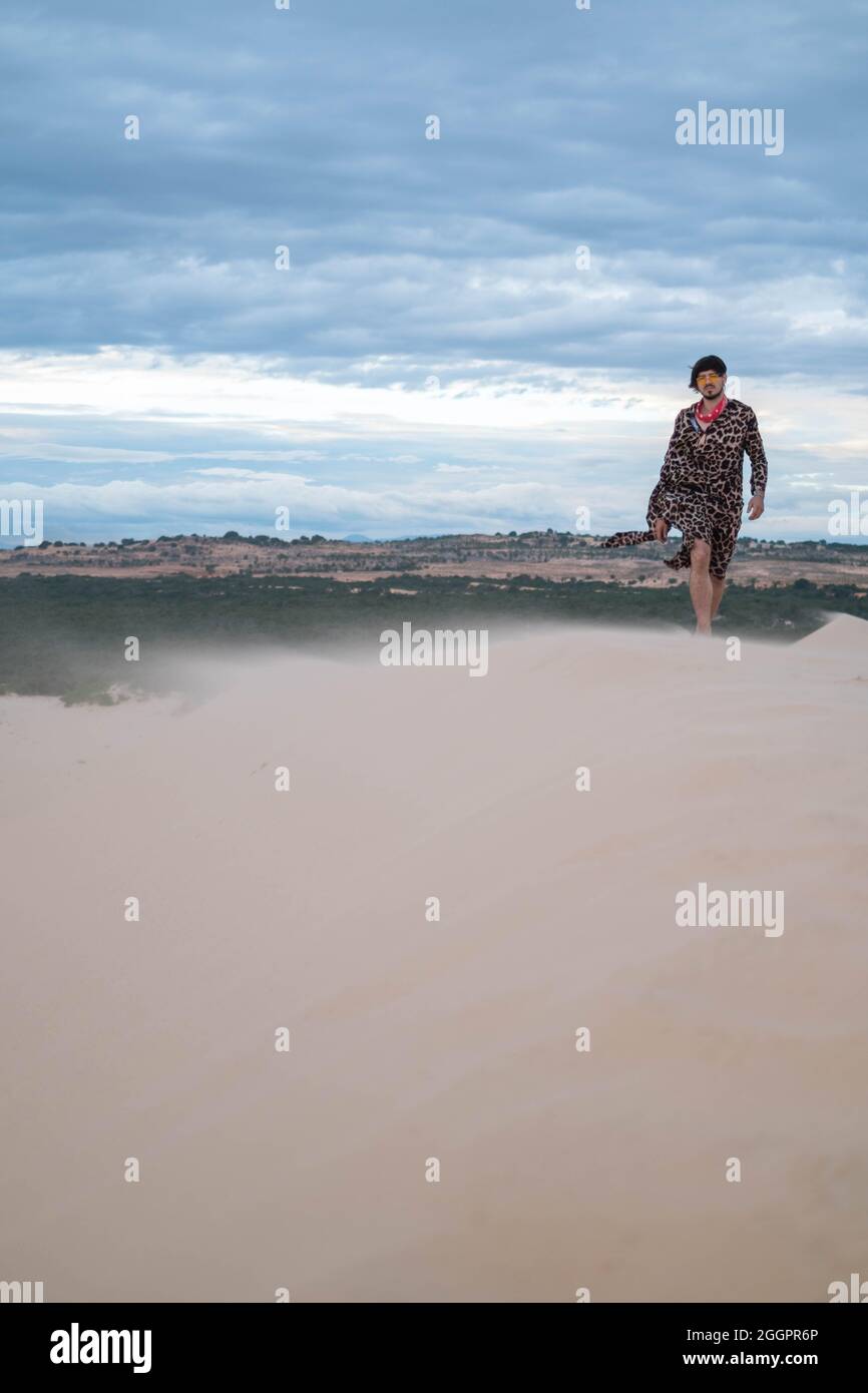 Jeune homme du caucase qui marche dans le désert. Jeune homme debout dans des dunes de sable blanc. Étranger dans le désert. Le sable vole dans le vent Banque D'Images