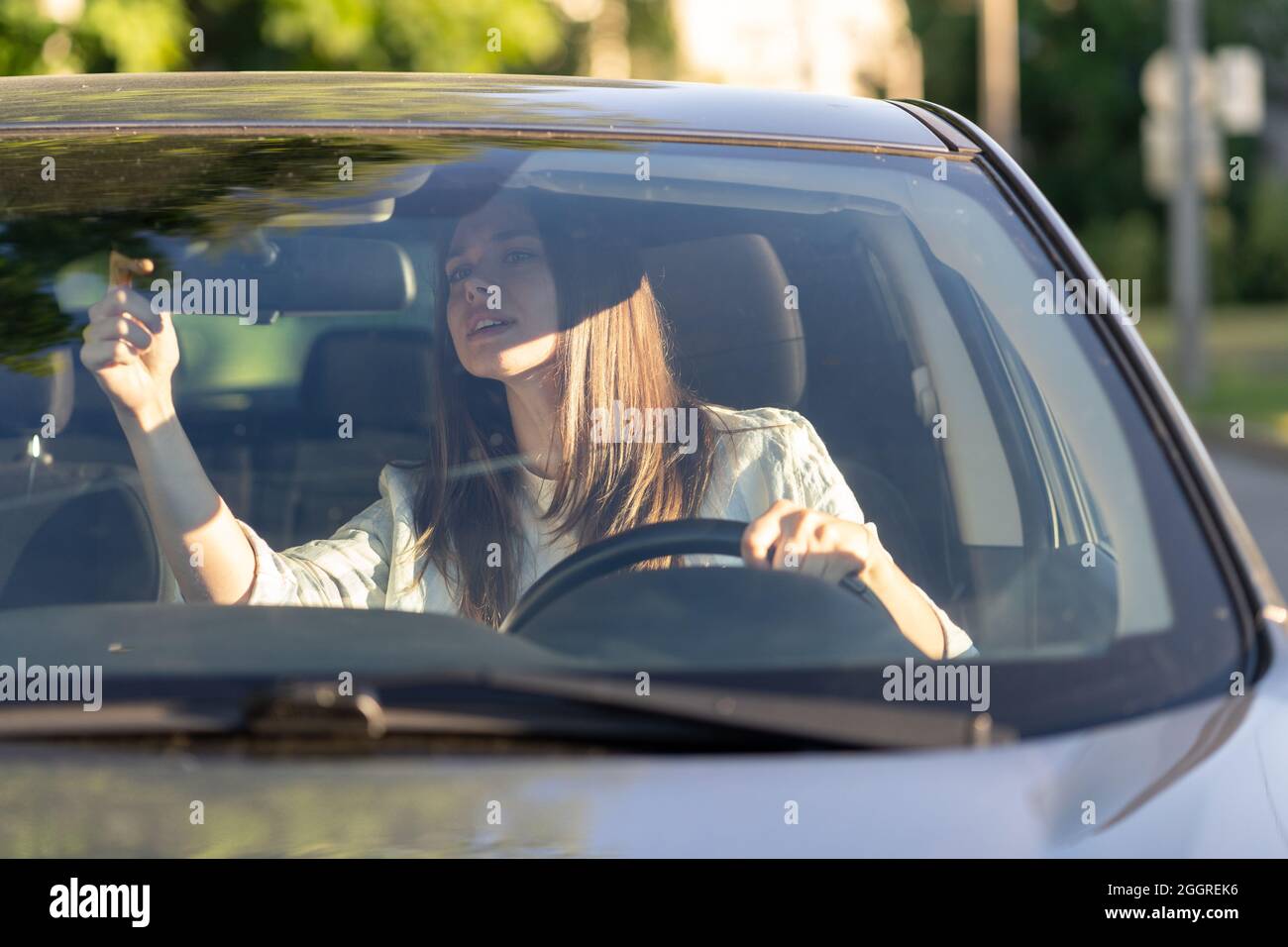 Jeune femme conducteur régler le rétroviseur intérieur de la voiture avant de tenir le volant Banque D'Images