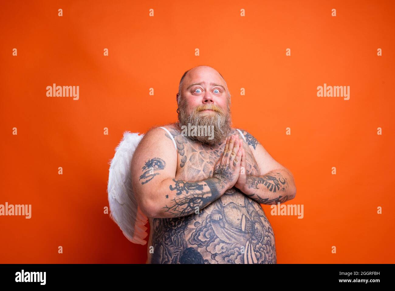 Gros homme peur avec la barbe, tatouages et ailes agit comme un ange Banque D'Images