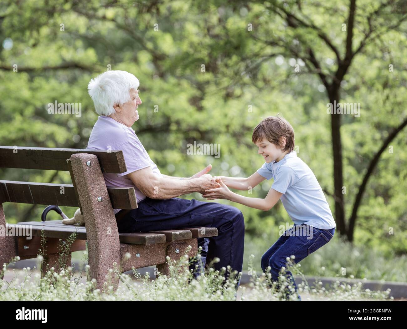 Homme mature et son granson jouant dans le parc d'été. Grand-père assis sur le banc, garçon tirant avec joie sa main. Banque D'Images
