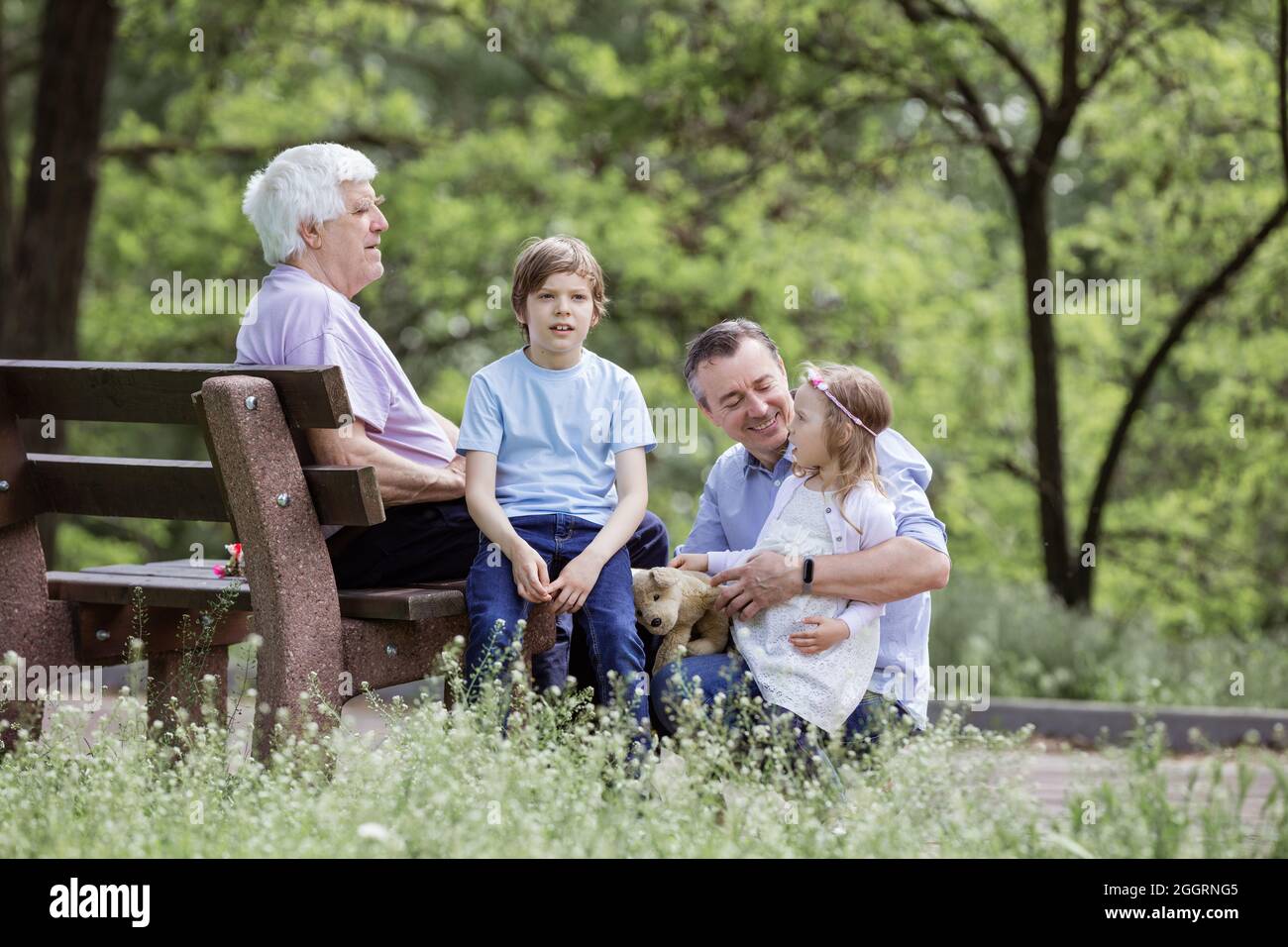 Famille de trois générations dans un parc d'été : grand-père assis à bord, père et petits-enfants Banque D'Images