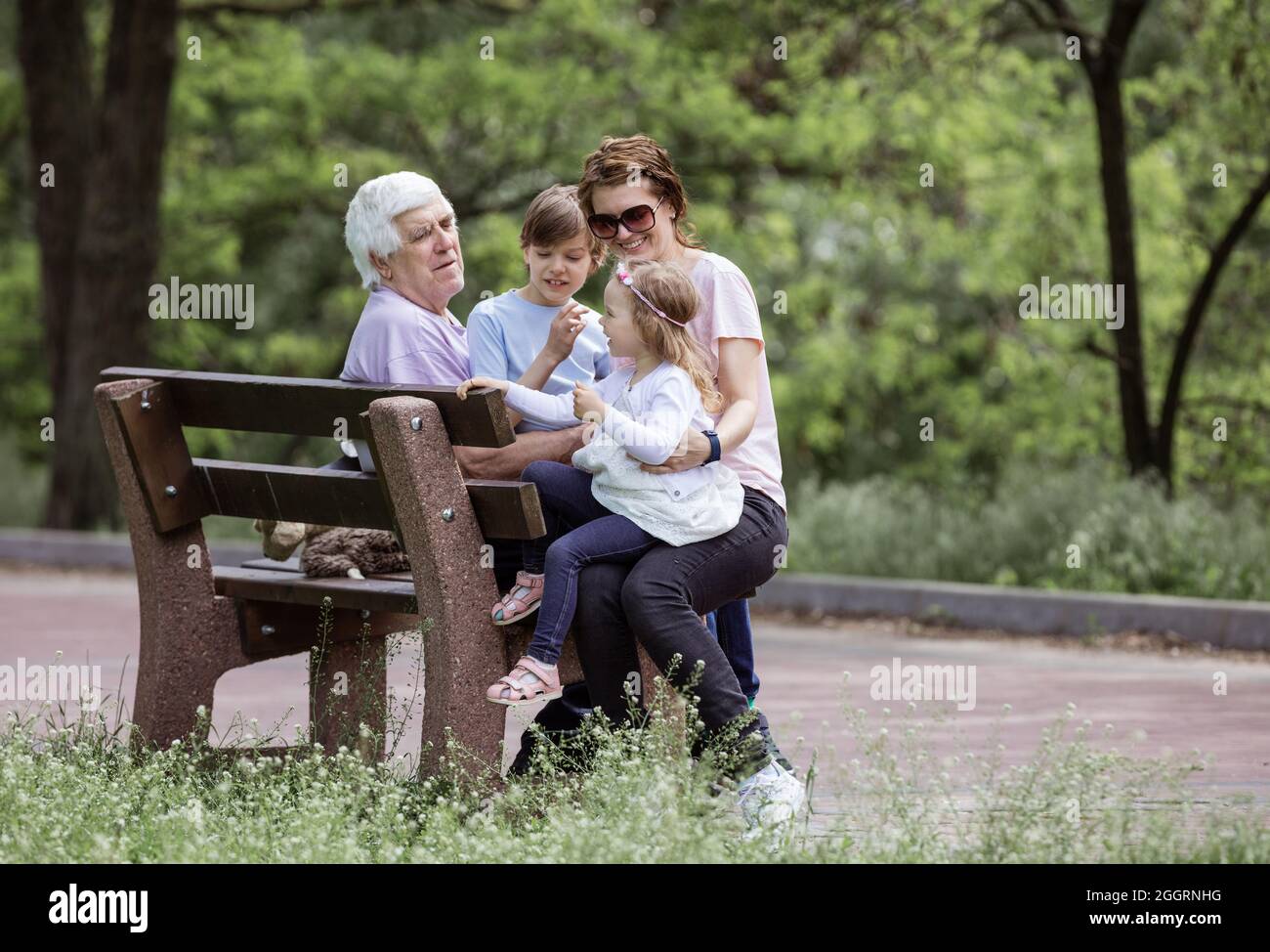 Famille de trois générations ayant le repos sur banc dans un parc d'été : grand-père, mère et petits-enfants Banque D'Images