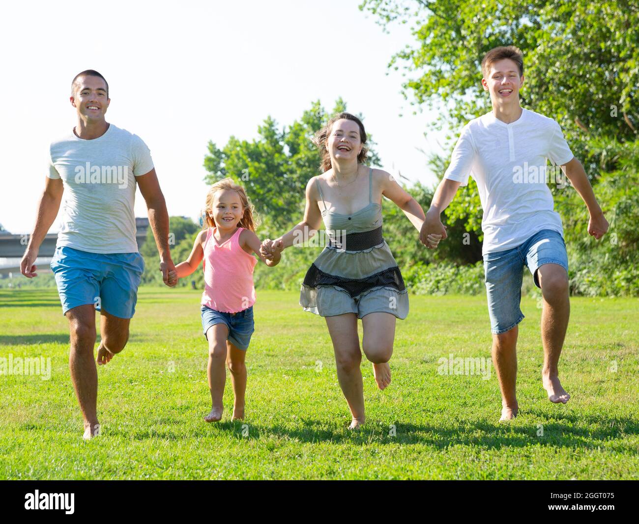 Bonne famille de quatre personnes qui s'exécutent sur l'herbe dans le parc d'été Banque D'Images