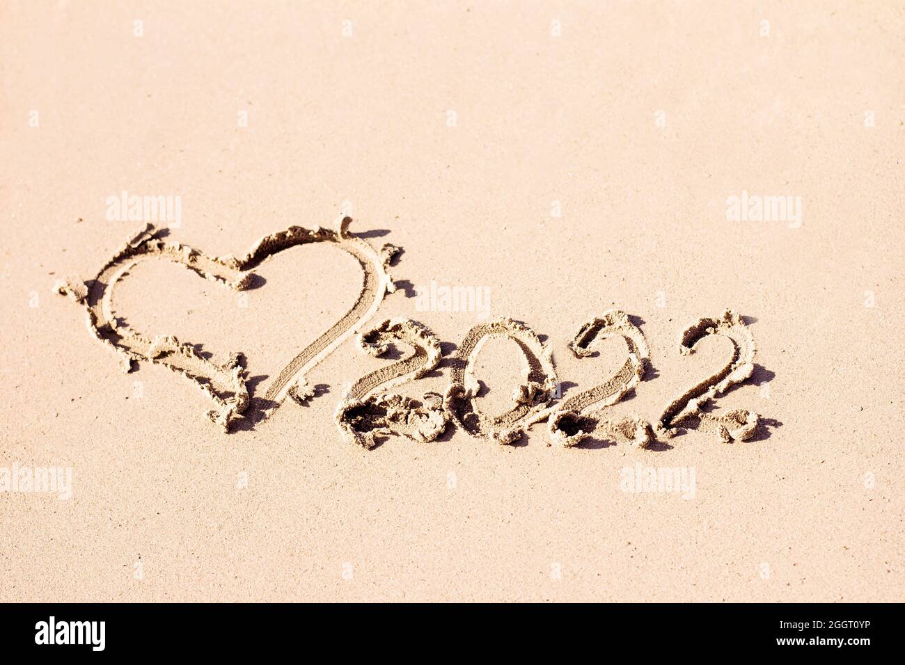 L'inscription 2022 et le coeur sont dessinés sur le sable clair. Symbole de la nouvelle année Banque D'Images