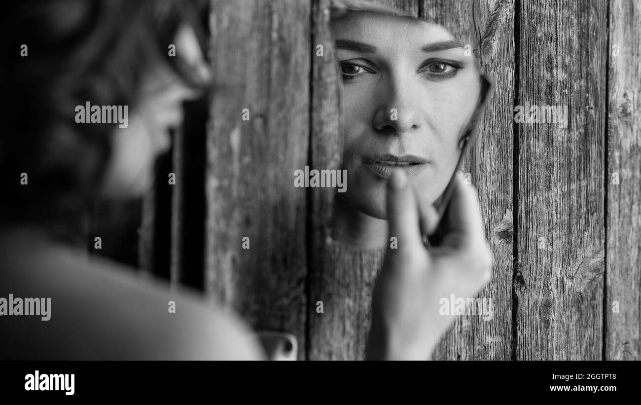 Portrait en niveaux de gris d'une femelle tenant un miroir cassé sur le fond en bois Banque D'Images