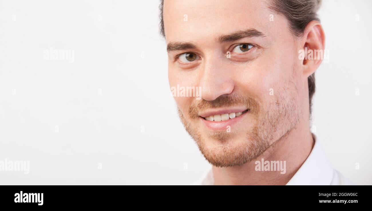Gros plan jeune homme beau homme avec barbe, souriant et regardant avec l'appareil photo. Homme posant en trois quarts. Photo avec espace de copie. Hor Banque D'Images