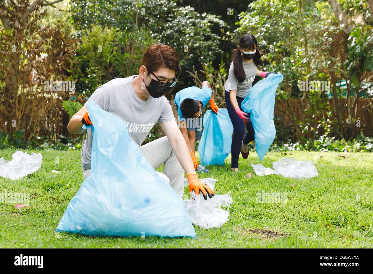 Parents asiatiques, fils et fille dans des masques de visage mettant des ordures dans des sacs de déchets dans la campagne Banque D'Images