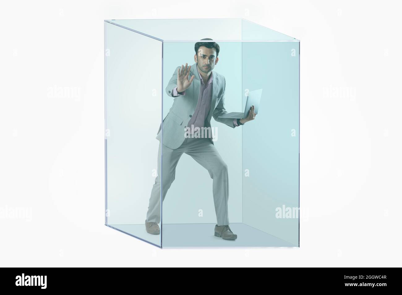 Portrait d'un homme en costume d'affaires formel tenant un ordinateur portable piégé dans un cube transparent. Banque D'Images
