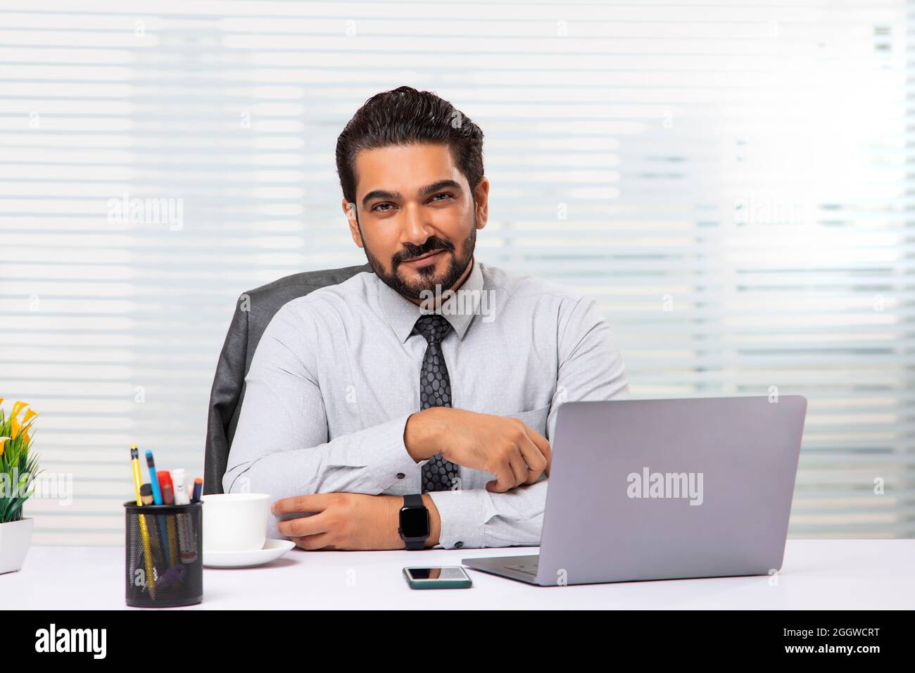Un employé assis dans son bureau regardant la caméra, souriant. Banque D'Images