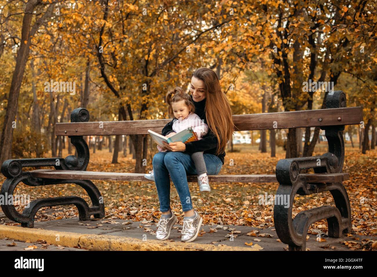 Jeune femme babysitter et petite fille de bébé lire livre dans le parc  d'automne. Famille heureuse maman et tout-petit à l'extérieur dans le parc  d'automne Photo Stock - Alamy