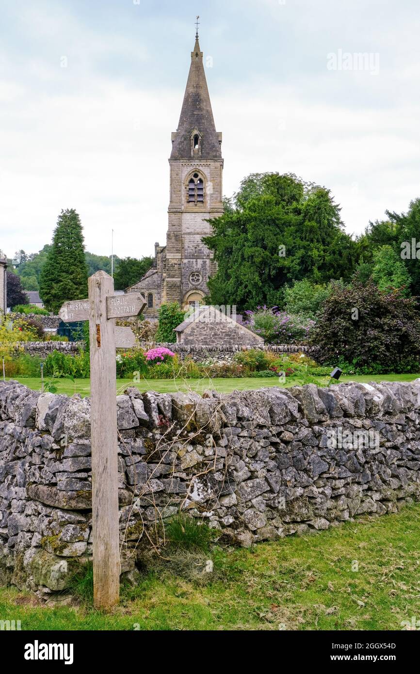 Une vue lointaine de l'église à Parwich avec un panneau de chemin de pied et un mur de pierre au premier plan. Banque D'Images