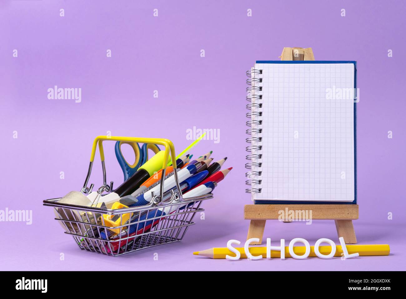 Panier en métal avec fournitures scolaires sur fond lilas. Concept de shopping scolaire. Banque D'Images