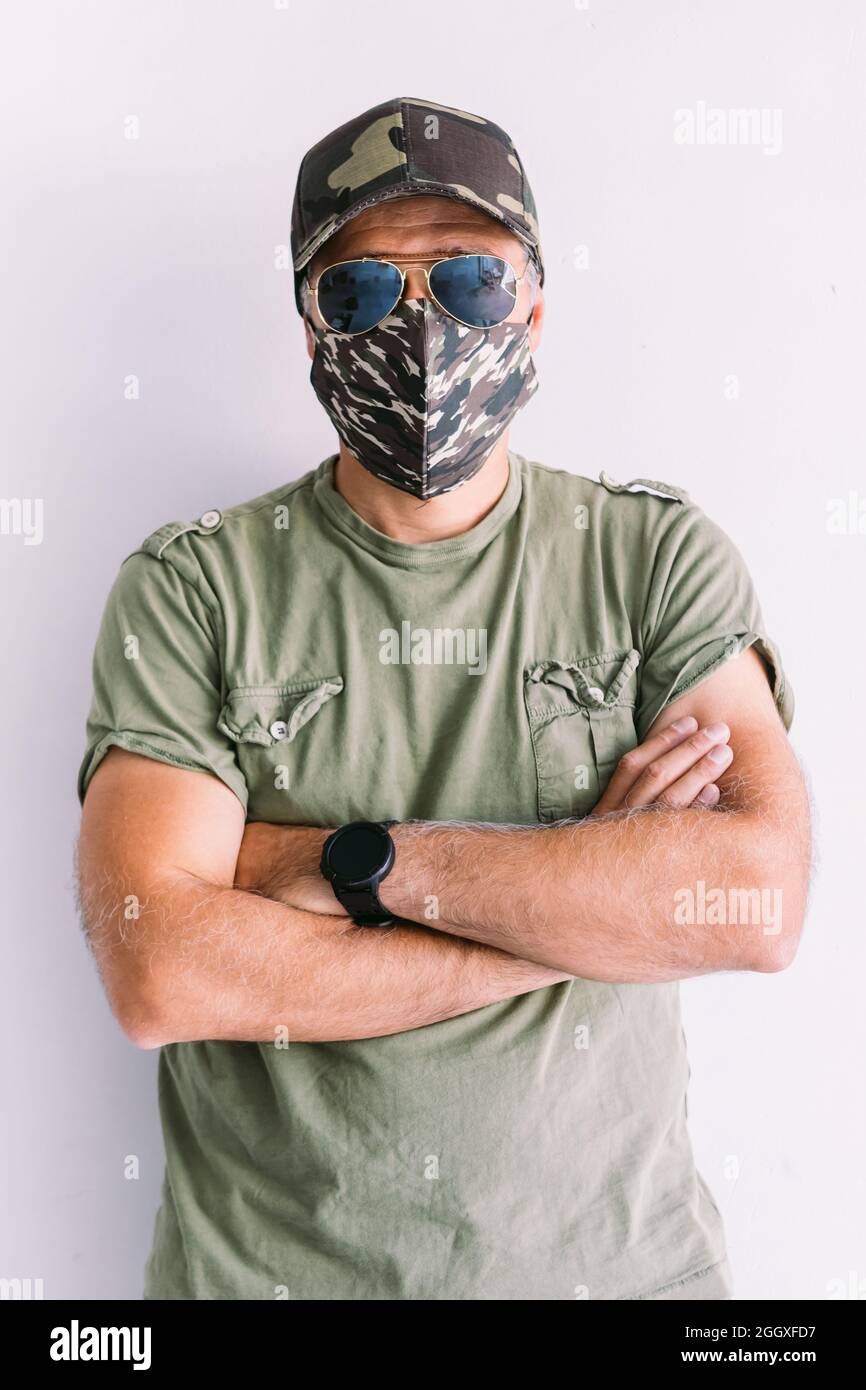 Militaire avec cagoule, lunettes de soleil et masque de camouflage, bras  croisés, sur un mur blanc Photo Stock - Alamy