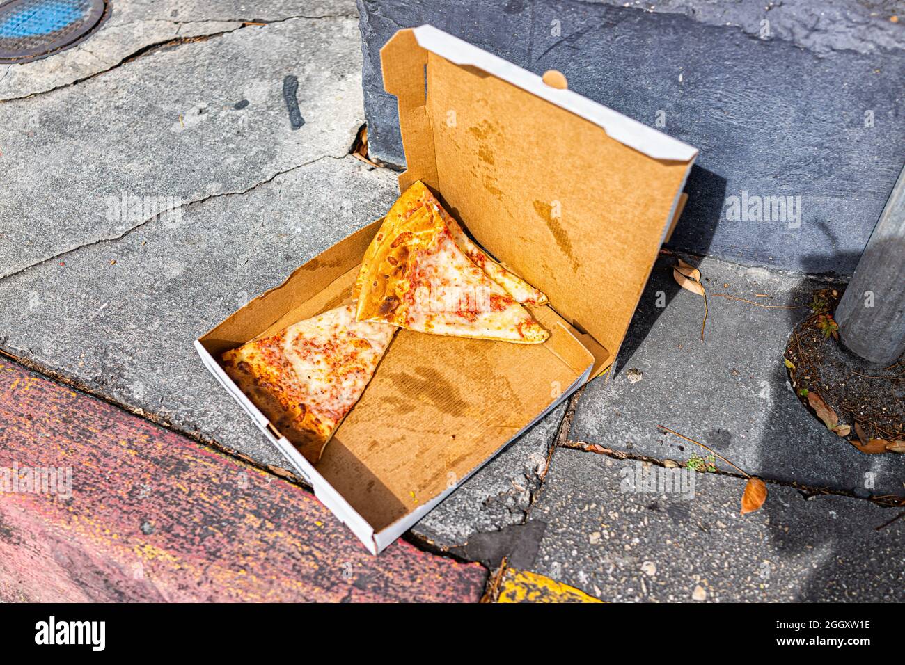 Laissé derrière jeté des tranches de pizza au fromage jetées dans une boîte à conteneurs sur le trottoir de la rue à l'extérieur des déchets alimentaires à Key West, Floride Banque D'Images