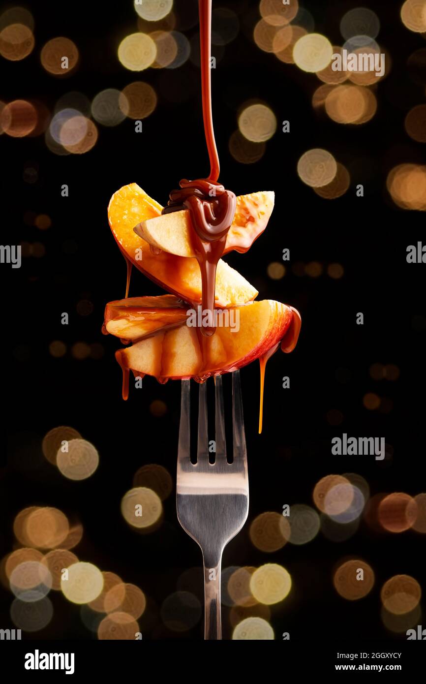 image conceptuelle des tranches de fruits de pomme avec caramel (cajeta) sur la fourchette métallique. Bokeh s'allume en arrière-plan. Gros plan Banque D'Images