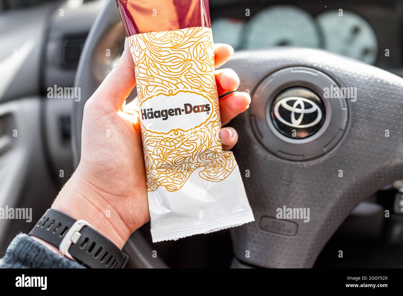 Greenville, Etats-Unis - 7 janvier 2021 : main de femme tenant une barre de glace au chocolat à la vanille achetée par Haagen-Dazs et signe avec le fond des voitures s. Banque D'Images
