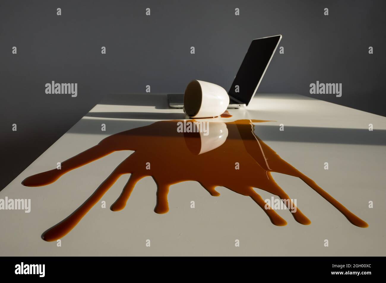 Une tasse de café noir a été renversé sur un ordinateur portable, sur un bureau blanc. Banque D'Images Une tasse de café noir a été renversé sur un ordinateur portable, sur un bureau blanc. Banque D'Images