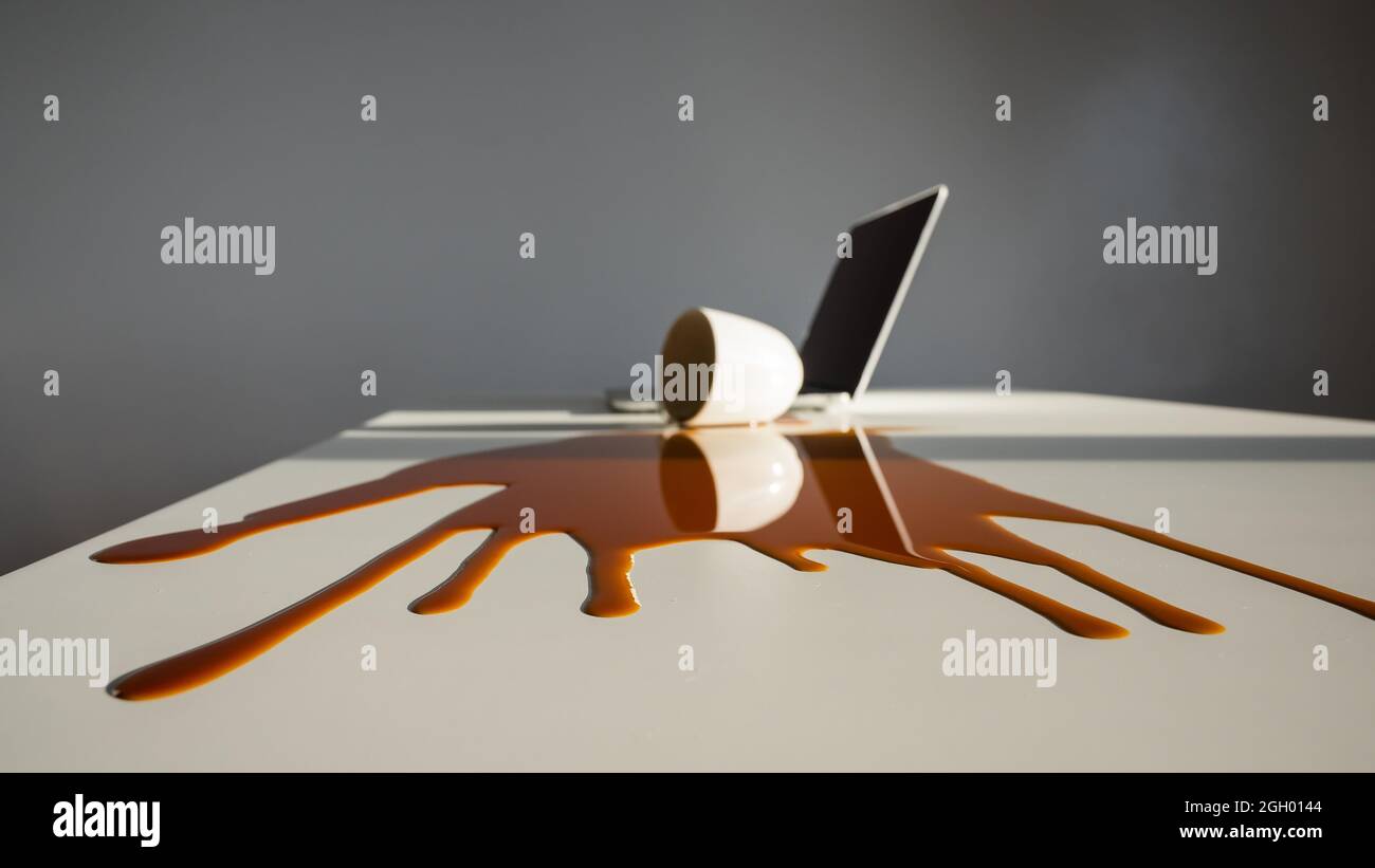 Une tasse de café noir a été renversé sur un ordinateur portable, sur un bureau blanc. Banque D'Images Une tasse de café noir a été renversé sur un ordinateur portable, sur un bureau blanc. Banque D'Images