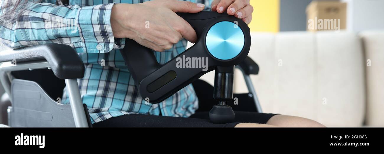 Femme handicapée en fauteuil roulant effectuant un massage des jambes avec un masseur à percussion gros plan Banque D'Images