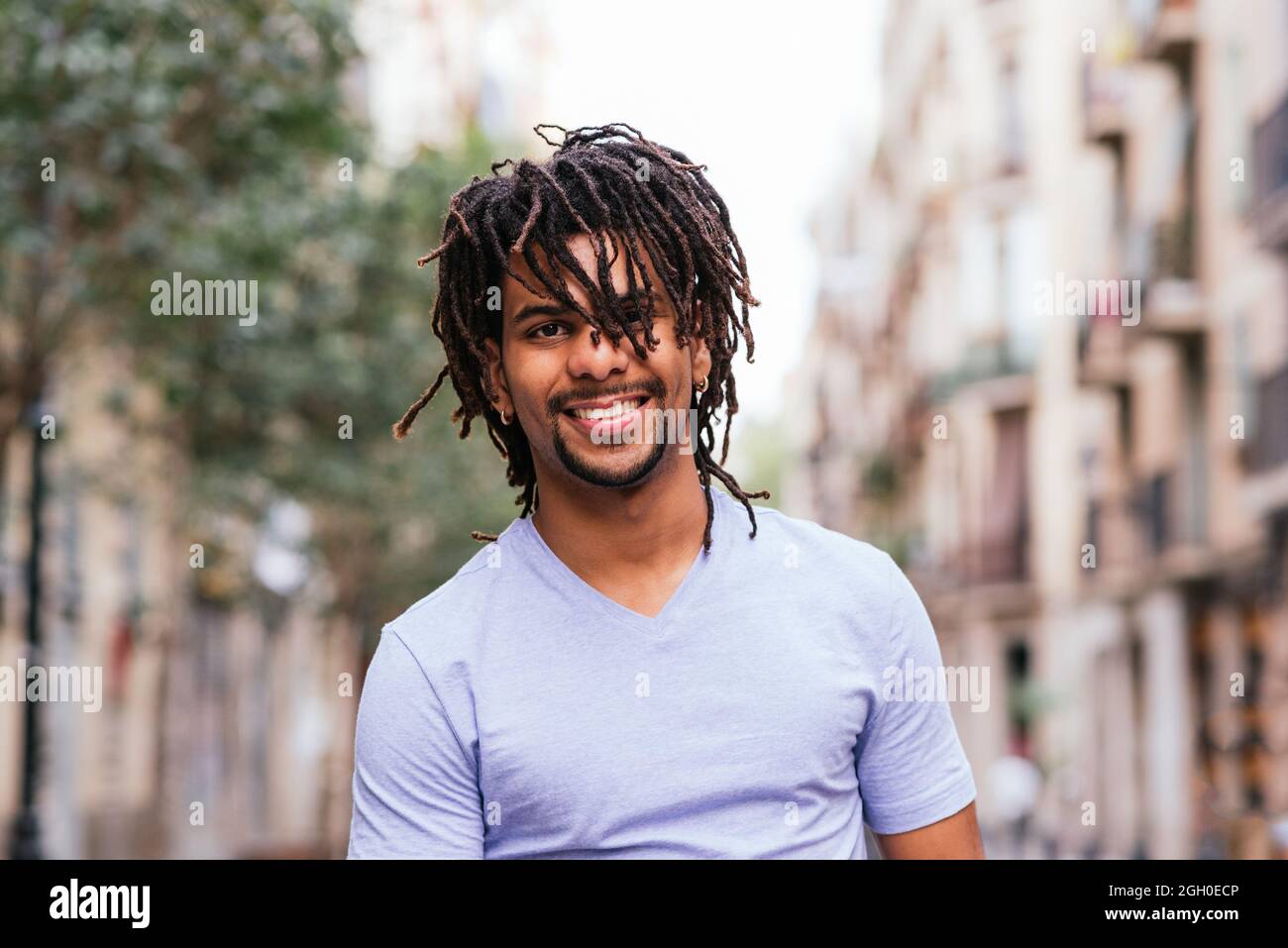 portrait horizontal d'un jeune homme hispanique avec des dreadlocks. Il regarde la caméra et sourit en marchant dans les rues de Barcelone Banque D'Images