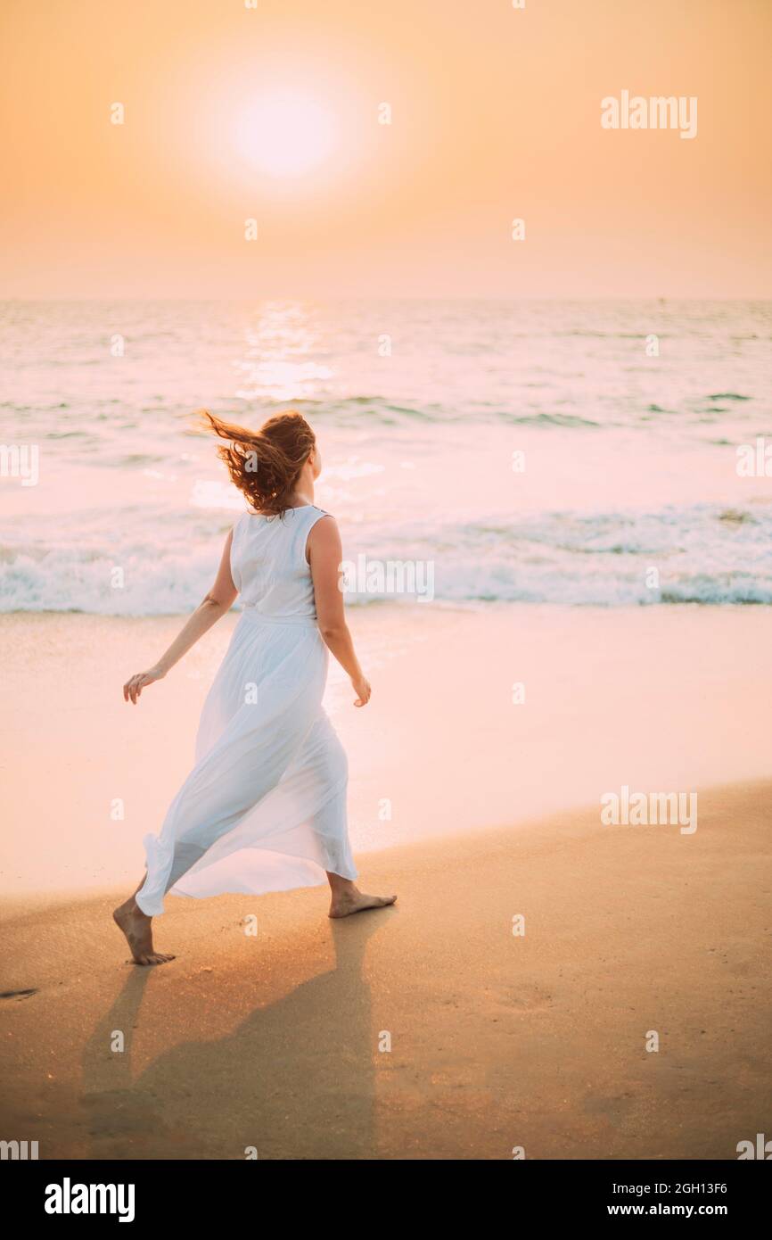 Goa, Inde. Jeune femme caucasienne avec des cheveux en luttering dans le  vent en robe blanche marcher le long de la mer en heure de coucher du  soleil Photo Stock - Alamy