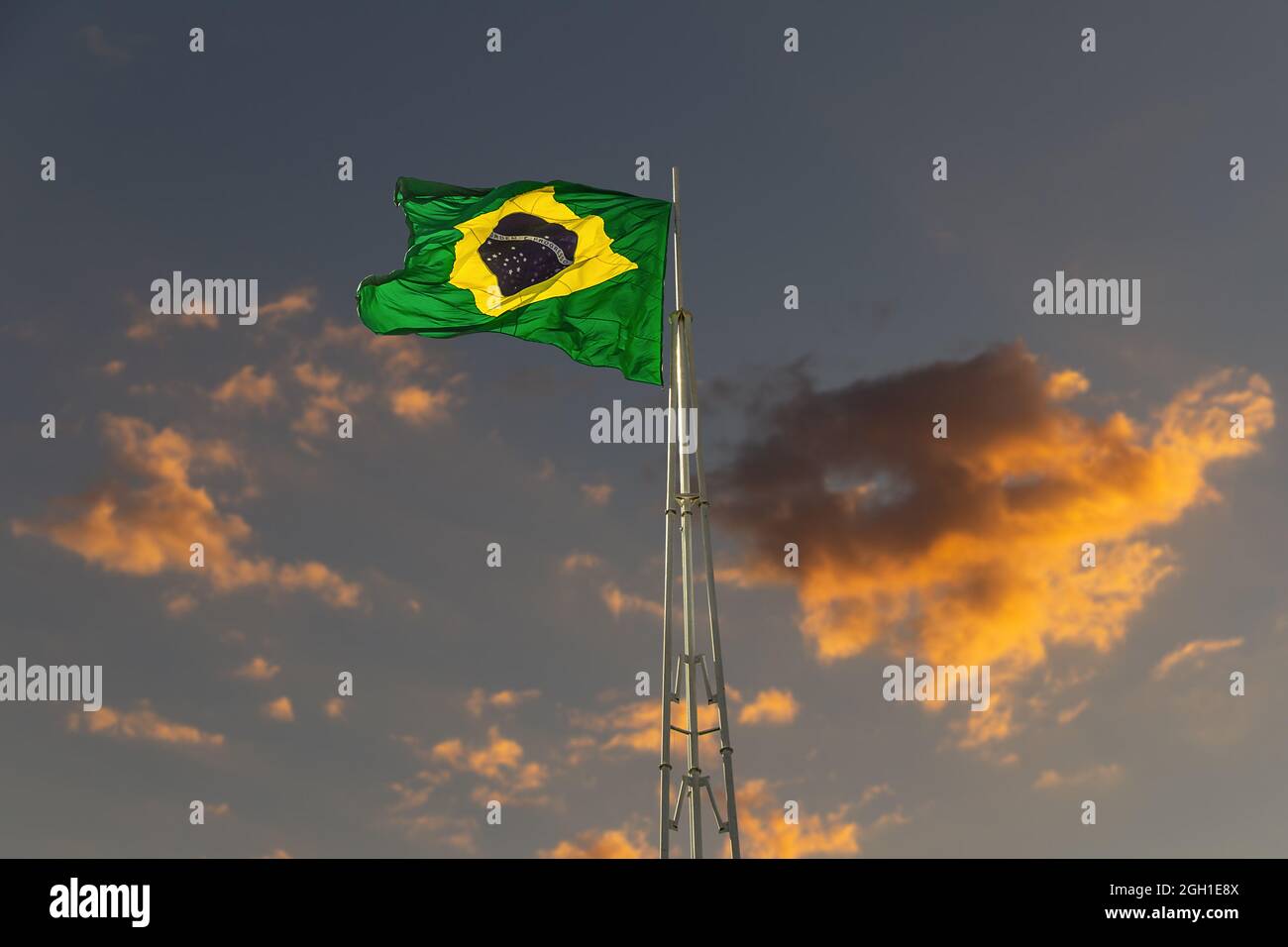 Drapeau brésilien volant et flottant dans le vent. Drapeau du Brésil hissé de ciel et de nuages au crépuscule en arrière-plan. Banque D'Images