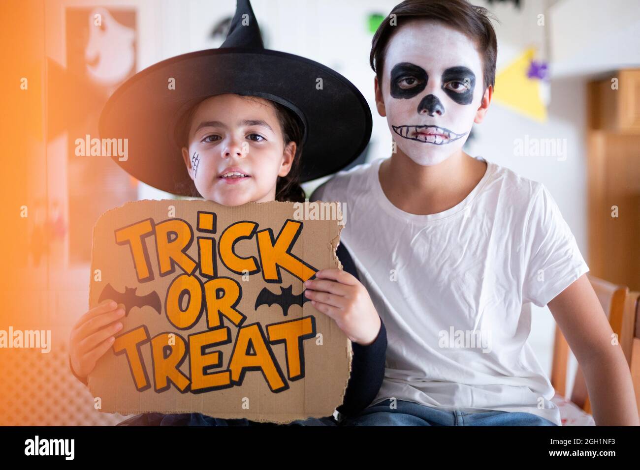 Garçon et petite fille habillée pour Halloween tenant une affiche avec le texte astuce ou traiter. Banque D'Images