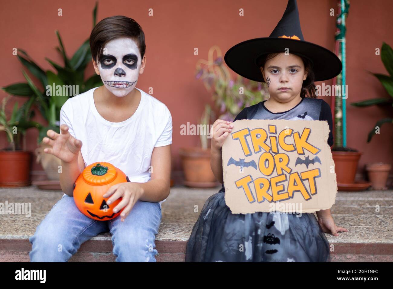 Garçon et fille en costumes typiques d'Halloween assis à l'entrée de leur maison. Banque D'Images