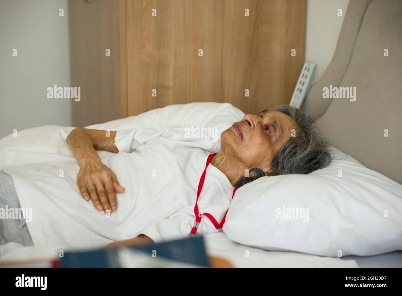 Femme asiatique indienne fragile, couchée au lit dans une chambre d'hôpital ou une maison de soins, Royaume-Uni. Banque D'Images