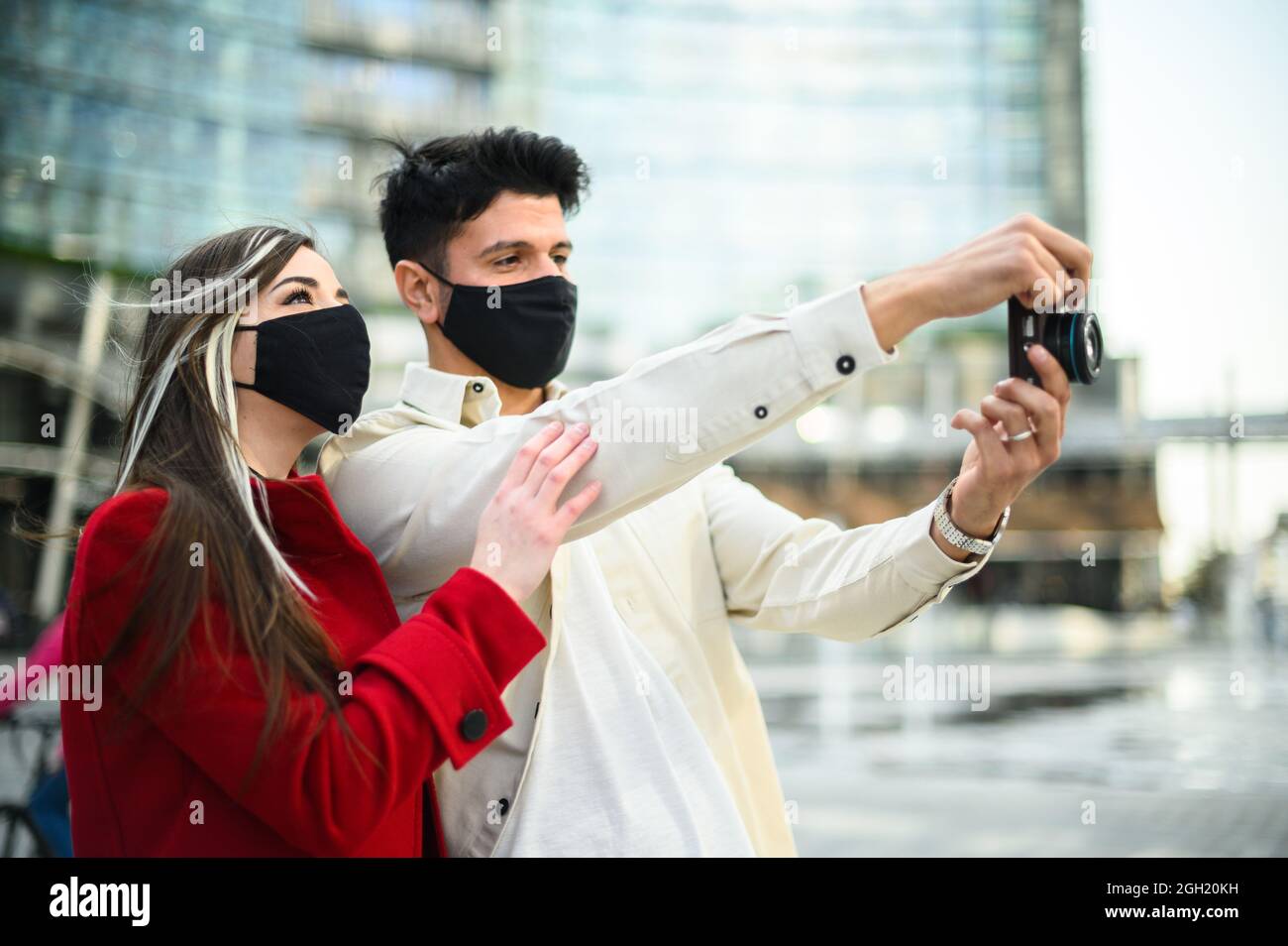 Les touristes heureux avec des masques covid ou coronavirus couple whalking ensemble dans une ville et photographier un endroit intéressant Banque D'Images